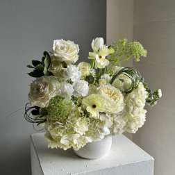 White floral arrangement in a white vase with roses and hydrangeas