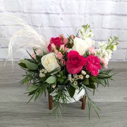 Pink and white rose bouquet in a white vase with feathery accents