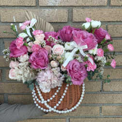 Pink and white rose arrangement in a wicker basket with pearl strands
