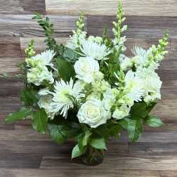 Arrangement of white roses, chrysanthemums, and snapdragons in a clear glass vase