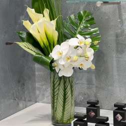 Tall arrangement of white orchids and pale yellow calla lilies in a glass vase