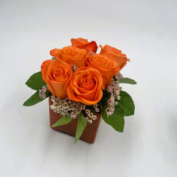 Orange roses arranged in a small brown square vase with pink filler flowers