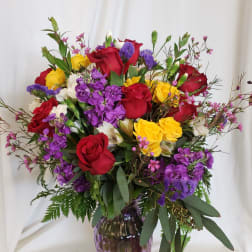 Mixed bouquet of red, yellow, and purple flowers in a purple glass vase