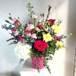 Mixed bouquet in a pink container with roses, hydrangea, and yellow blooms