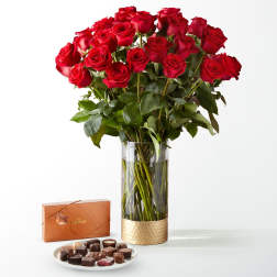 Red roses in a glass vase with a box of chocolates and a plate of candies