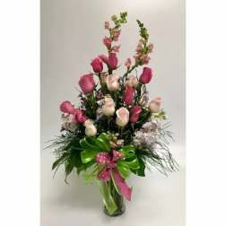 Tall bouquet of pink and white roses in a glass vase with a ribbon bow