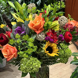 Mixed bouquet with roses, lilies, sunflowers, and hydrangeas in a glass vase