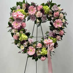 Heart-shaped floral wreath with pink flowers and a ribbon on a stand