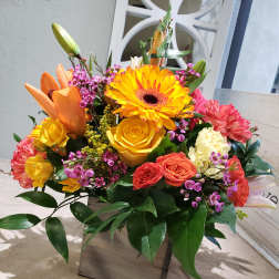 Bright mixed bouquet with gerbera daisies, roses, and carnations in a square vase