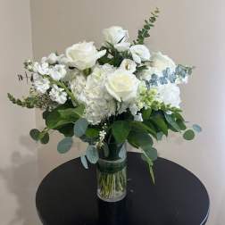 White roses and hydrangeas with eucalyptus in a clear glass vase on a round black table