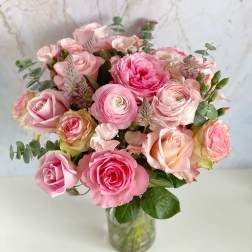 Pink roses and ranunculus arranged in a clear glass vase