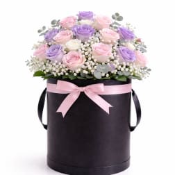 Pink and lavender roses in a black hat box with a pink ribbon