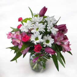 Bouquet of white daisies, pink alstroemeria, and purple tulips in a glass vase