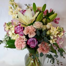 Pastel bouquet of lilies, roses, carnations, and mixed flowers arranged in a clear glass vase