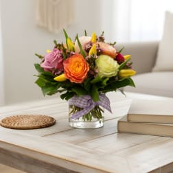 Colorful bouquet of roses and tulips in a glass vase with a purple ribbon