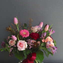 Pink roses and mixed blooms arranged in a glass vase with a red ribbon