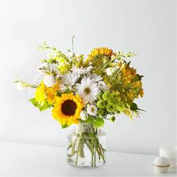 Bouquet of sunflowers, white daisies, and yellow flowers in a clear glass vase