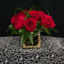 Red roses arranged in a gold square vase with green foliage