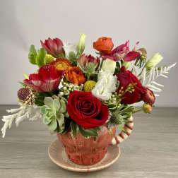 Colorful mixed flower arrangement in a red teacup vase