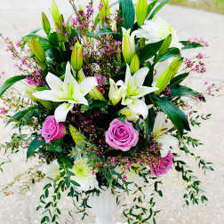 White lilies and pink roses arranged in a white pedestal vase