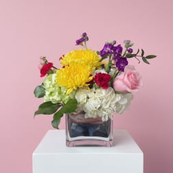 Mixed bouquet in a square glass vase with yellow, pink, white, and purple flowers