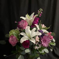 Bouquet of white lilies, pink roses, and purple blooms in a glass vase
