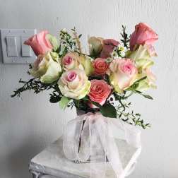 Pink and cream roses arranged in a vase with a sheer ribbon bow