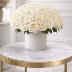 Dome of cream roses arranged in a white round vase on a marble table