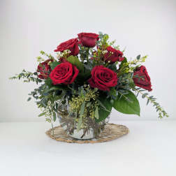 Red roses arranged in a clear glass vase with greenery