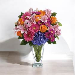 Mixed bouquet of pink, orange, and blue flowers in a clear glass vase