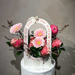 Pink gerbera daisies and roses arranged in a white gift bag with a ribbon handle.