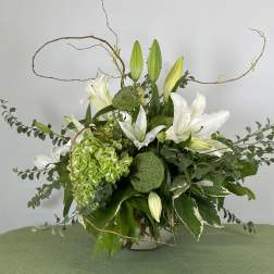 White lilies and green hydrangea in a glass vase with curly branches