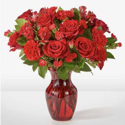 Red roses and carnations arranged in a red glass vase