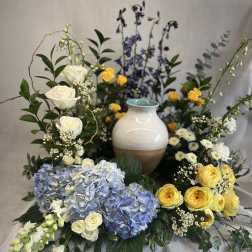 Floral arrangement with blue hydrangeas, yellow roses, and white roses around a ceramic vase
