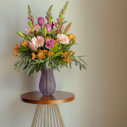 Mixed pink and orange flower arrangement in a purple vase