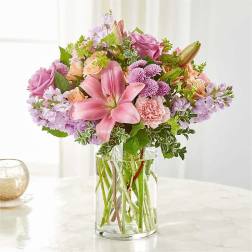 Mixed bouquet of pink lilies, roses, carnations, and lavender flowers in a clear glass vase