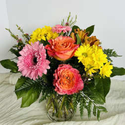 Mixed bouquet of pink, yellow, and orange flowers in a clear glass vase