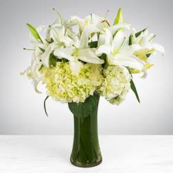 White lilies and pale hydrangeas arranged in a tall green glass vase.