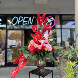 Tall arrangement of red anthuriums and pink flowers in a metallic vase