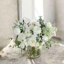White roses and mixed white blooms arranged in a clear glass vase