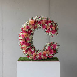 Floral letter C covered in pink, peach, and white flowers on a pedestal