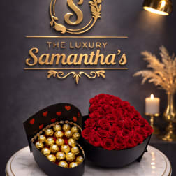 Heart-shaped box of red roses beside a box of gold-wrapped chocolates