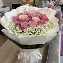 Pink roses wrapped in white paper with baby's breath and a ribbon