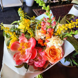 Bright mixed bouquet with pink, orange, yellow, and cream flowers wrapped in white paper