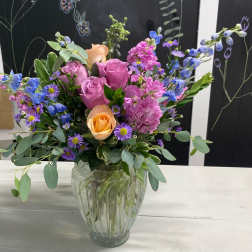Mixed bouquet of pink, peach, and blue flowers in a glass vase