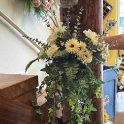 Cream daisy bouquet with trailing ivy and greenery on a wooden post