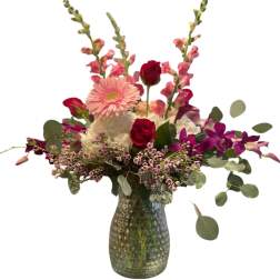 Pink and red mixed flower arrangement in a green glass vase
