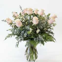 Blush pink roses in a clear glass vase with mixed greenery