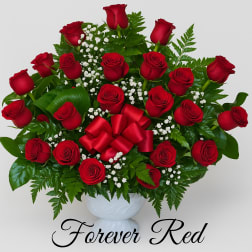 Red roses arranged in a white vase with a red ribbon bow