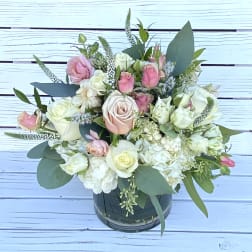 Low arrangement of white and blush roses and hydrangeas in a clear glass cylinder vase